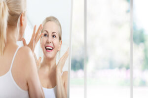 Smiling woman looking happily at her face in the mirror after getting Fotona Laser Facelift treatment