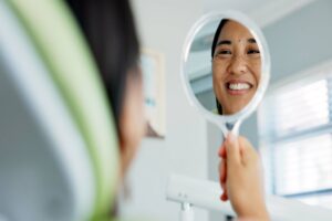 Happy woman looking at her smile in the mirror after getting Botox to correct her gummy smile