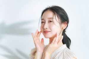 Smiling young woman with glowing skin, touching her face after receiving advanced skin care treatments